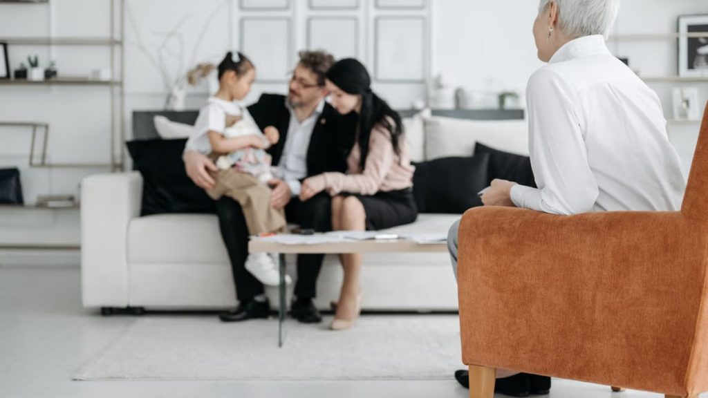 A joyful family adoption meeting with a social worker observing a couple embracing their new child.